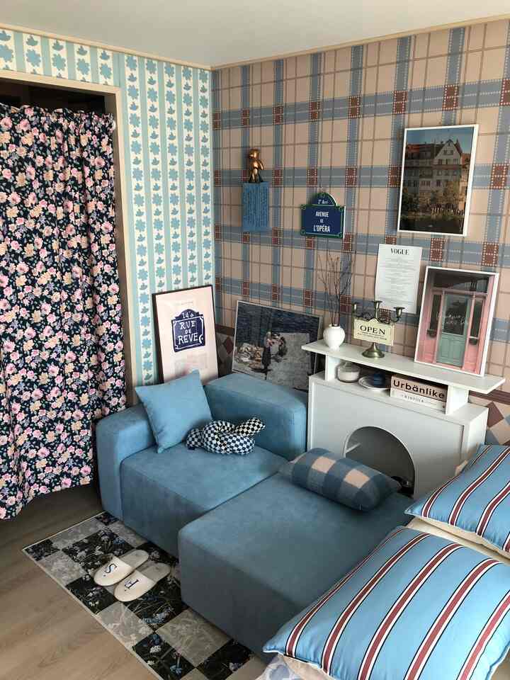 Living room with soft blue and natural-toned walls and sofa, accented by posters and a rug creating a cozy atmosphere