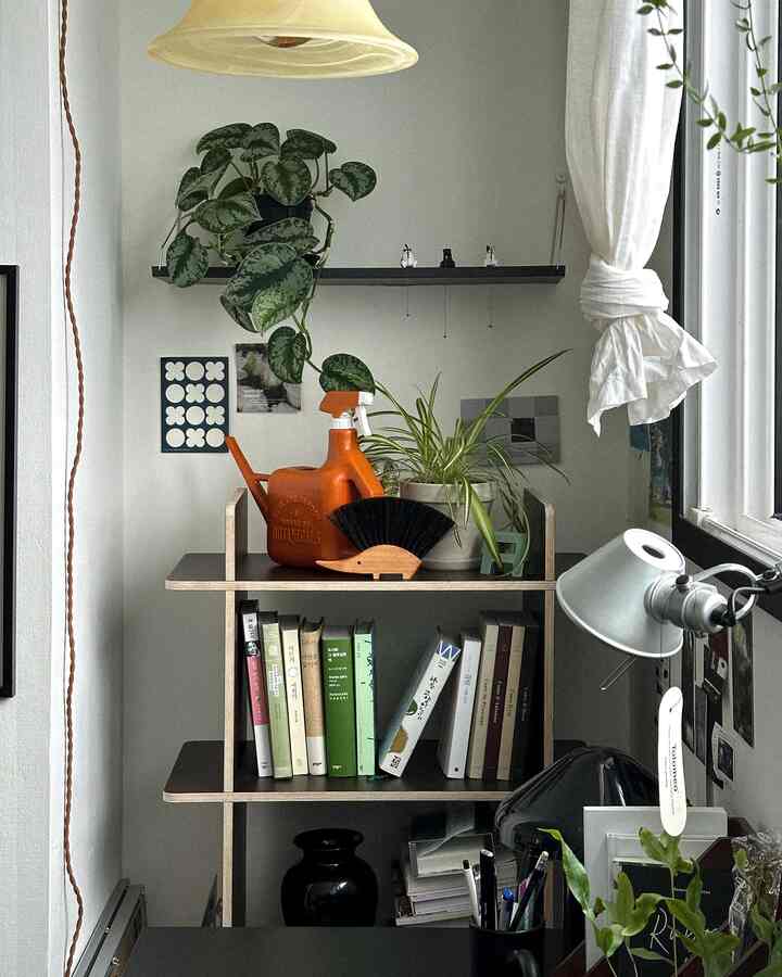 ホワイトとブラウン調のデスク横に小さな本棚と植物が配置された雰囲気のあるホームオフィス空間