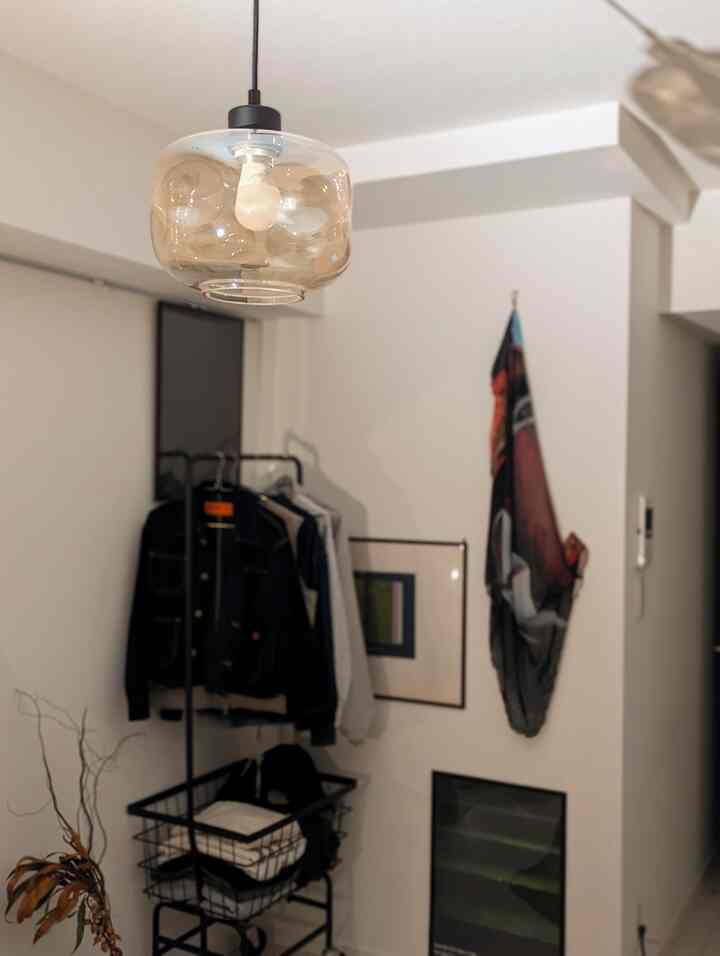 明るいホワイトトーンの壁と天井に透明なペンダントライトがあり、黒いコートハンガーに服が掛けられた整った玄関スペース