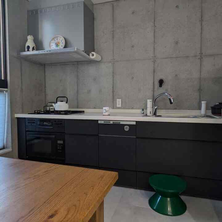 Simple kitchen with gray concrete wall and black cabinets, featuring a wood tone dining table and a green stool as accent elements