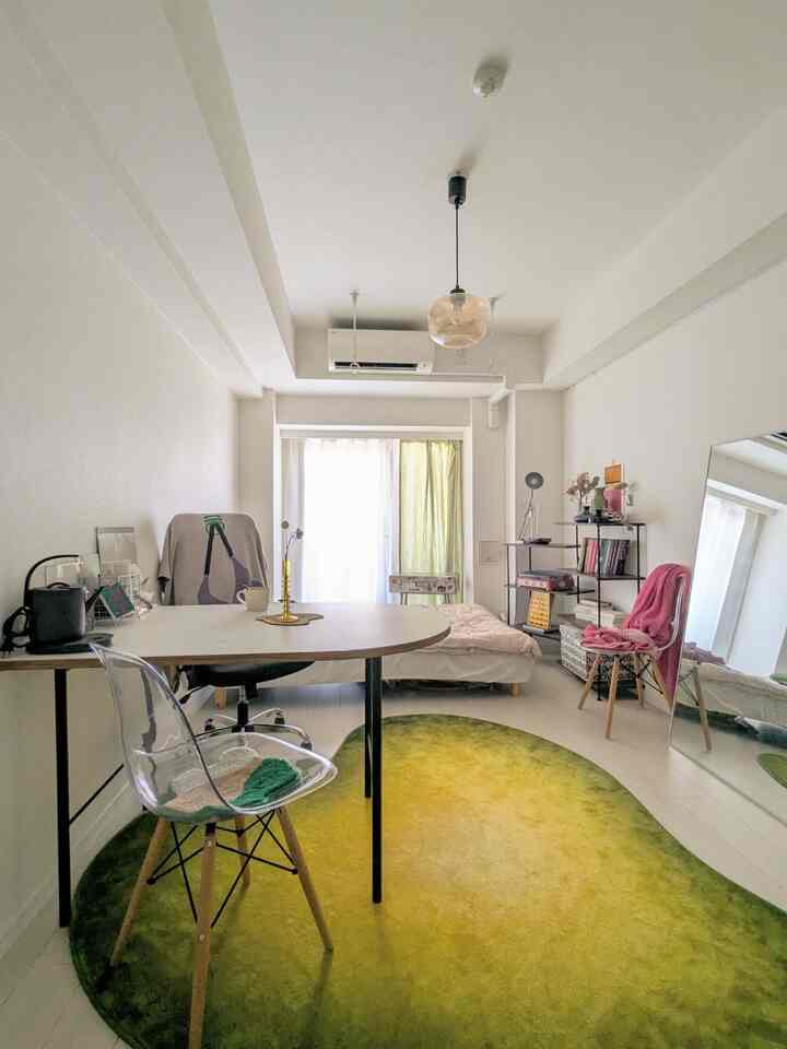 White and green toned compact bedroom featuring transparent chair and gradient rug with natural home office setup