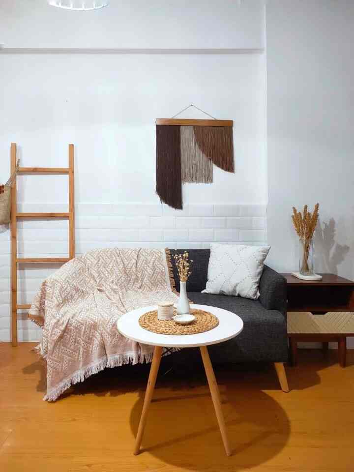Natural living room with white walls and wood tone flooring featuring a dark gray sofa with blanket and cushion, and a round white coffee table