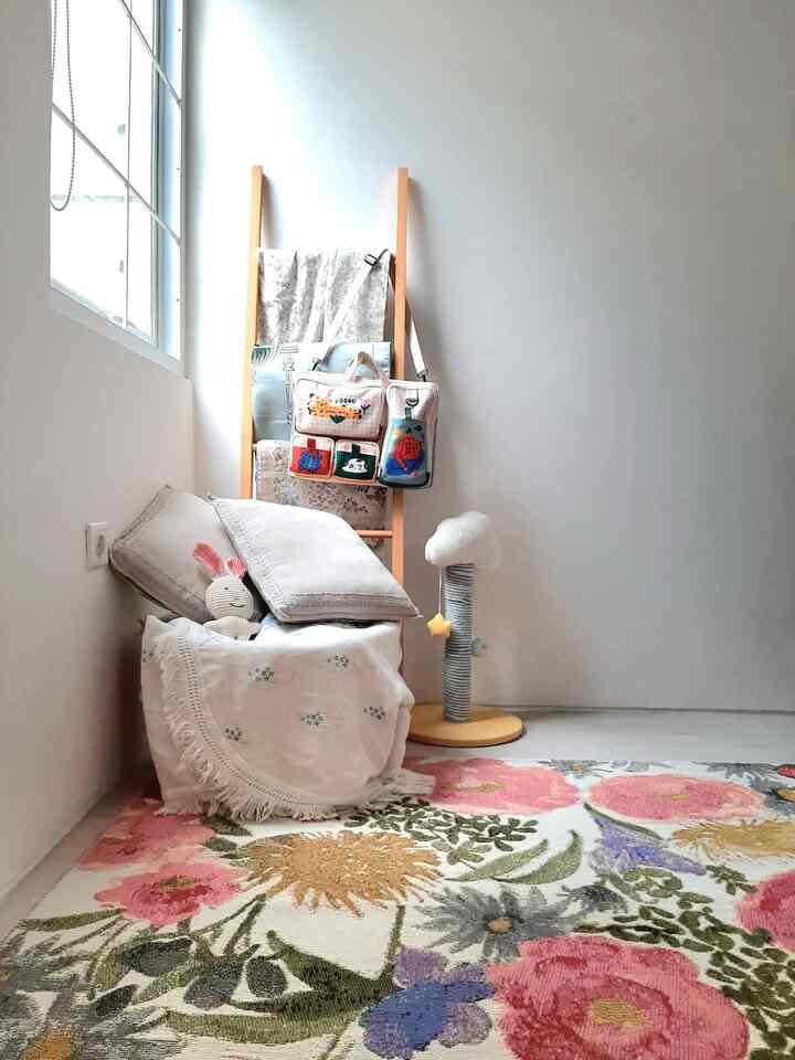 Bright white and natural-toned compact room featuring cushions, floral rug, and a cat scratching post near a large window for a cozy atmosphere