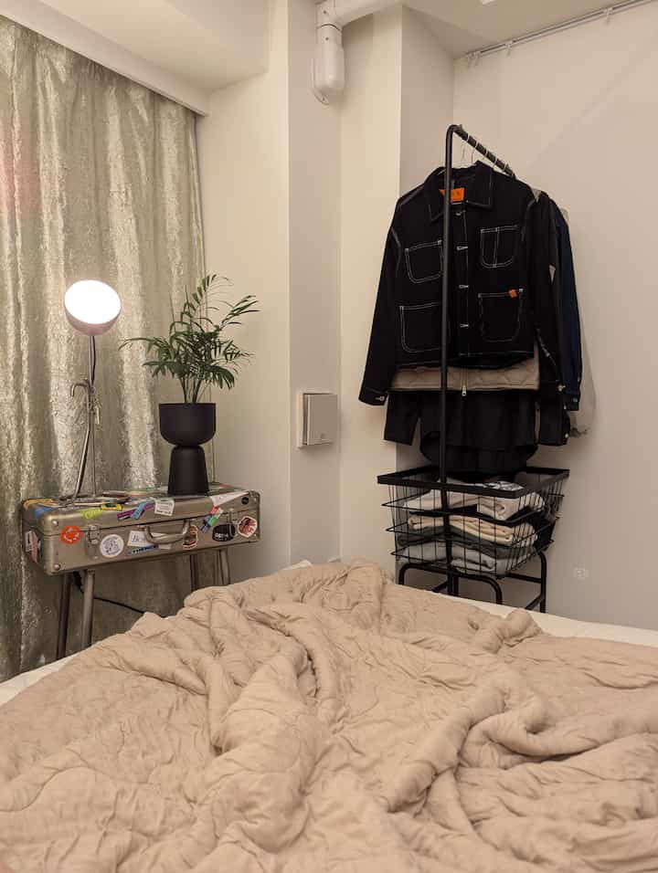 ベージュとホワイトの色調の狭いワンルーム寝室、ブラックのラックとフロアランプが配置されたシンプルな空間