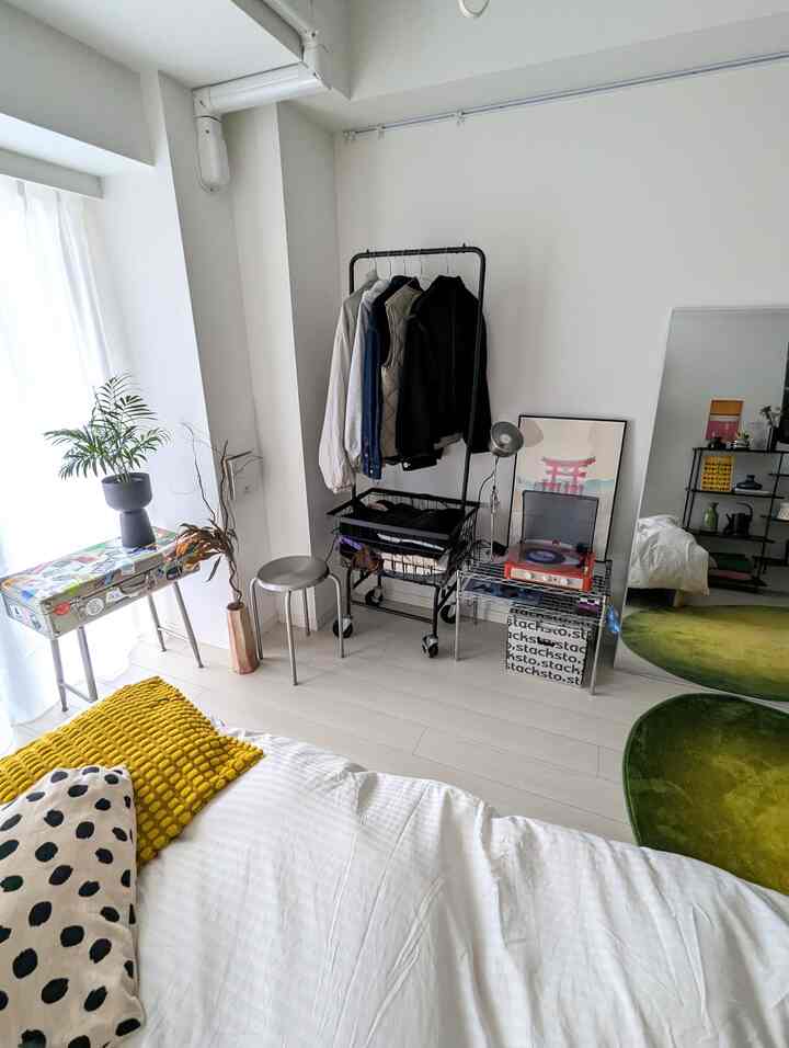 White-based bedroom featuring a central metal stool and open clothes rack with clean, modern decor