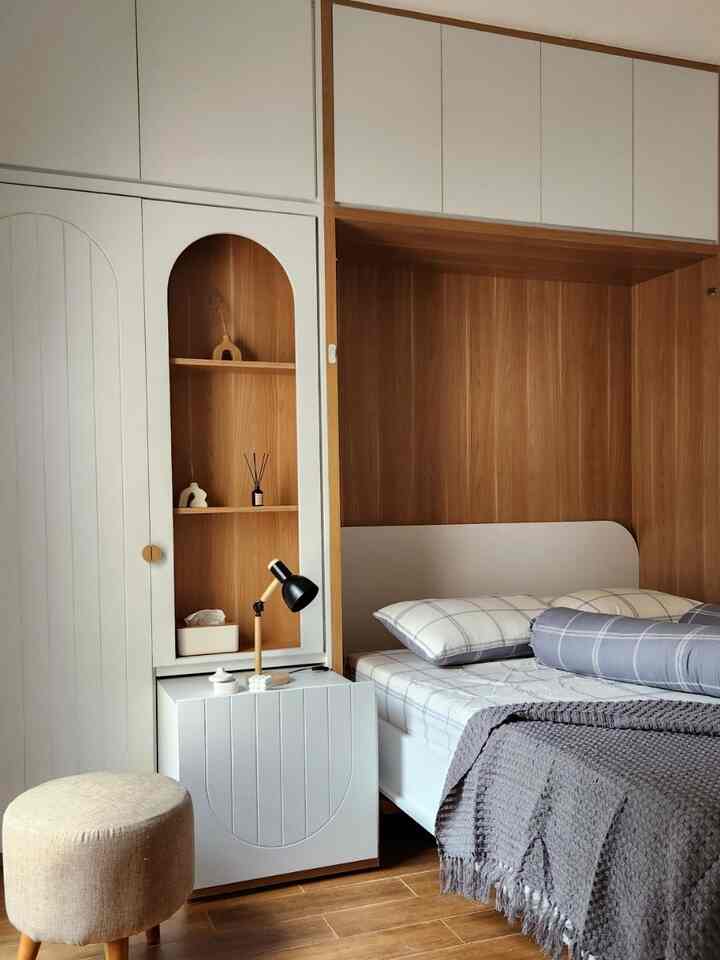 White and wood tone bedroom featuring a Murphy bed and natural storage cabinets in a compact, warm atmosphere
