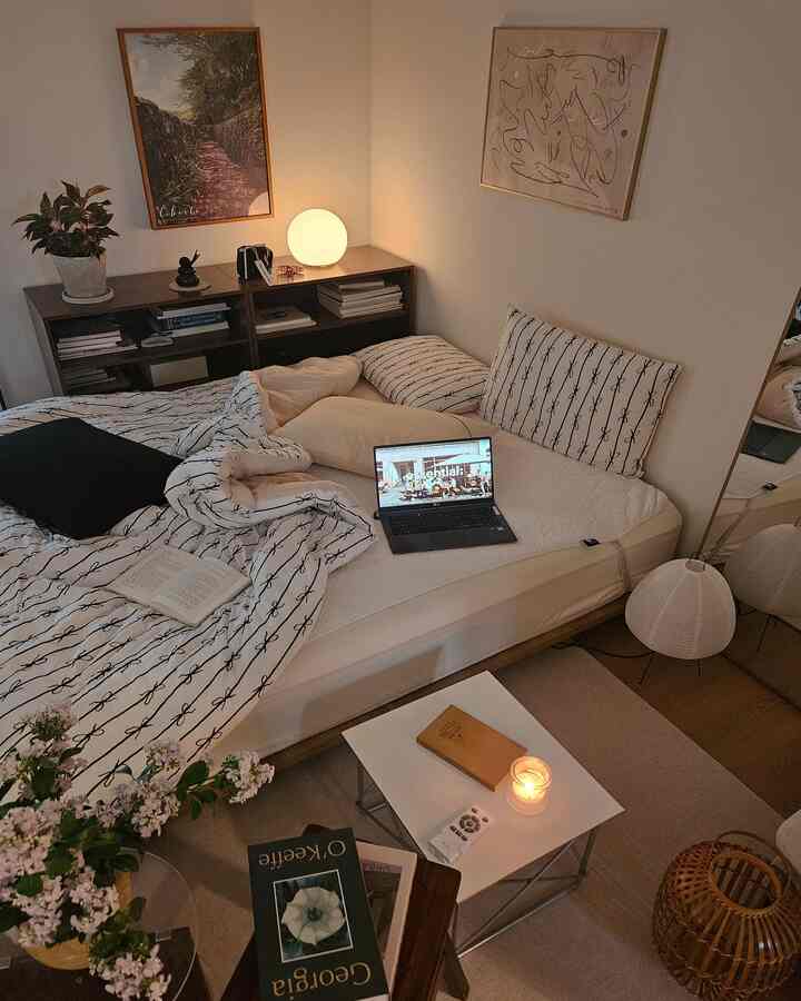 White and wood tone bedroom featuring bed, bookshelf, mood lamp, and candle creating cozy atmosphere