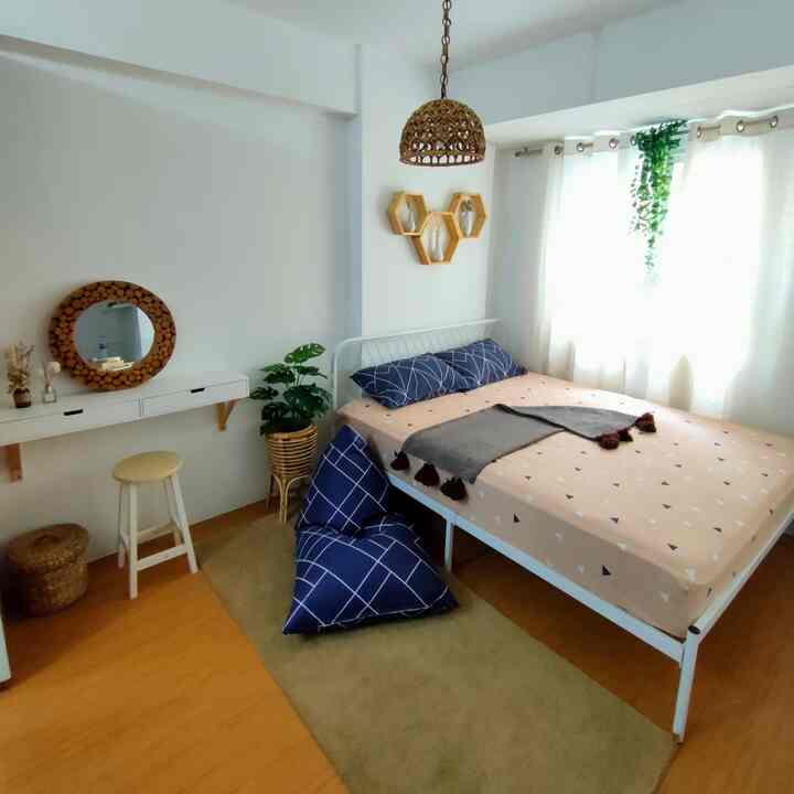 White and wood-toned small bedroom featuring a minimal bed, blue cushions, and bright curtains creating a cozy, clean space
