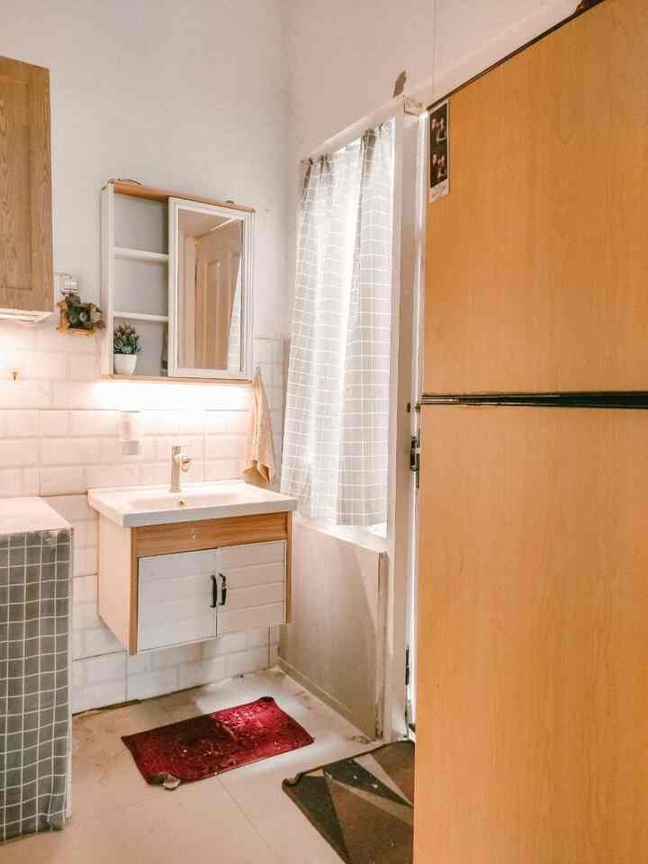 Small bathroom featuring white and wood tones, stylish storage cabinets, and window curtain, creating a neat and bright space