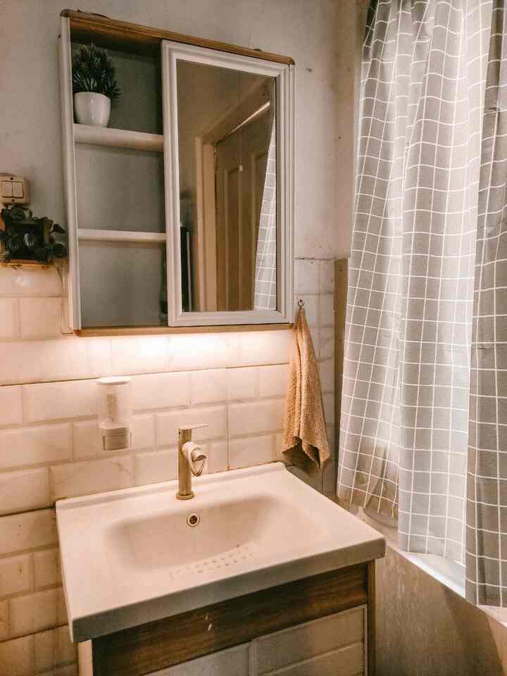 White and natural toned bathroom space featuring a storage mirror, sink cabinet, and checkered shower curtain with cozy ambiance