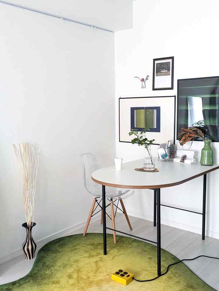 白と緑のトーンのダイニングルーム、透明なダイニングチェアとテーブル、緑のラグと花瓶が配置されたシンプルでモダンなインテリア