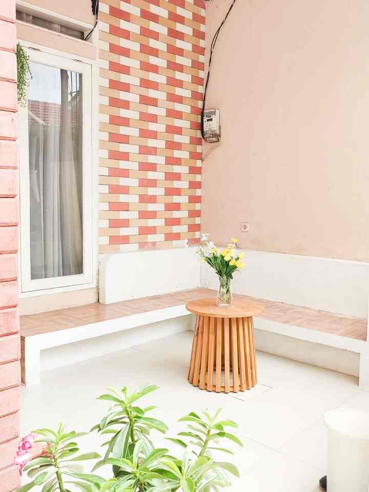 A small beige wall veranda space with white tiled floor featuring a round wood-toned coffee table with a vase of flowers centrally placed