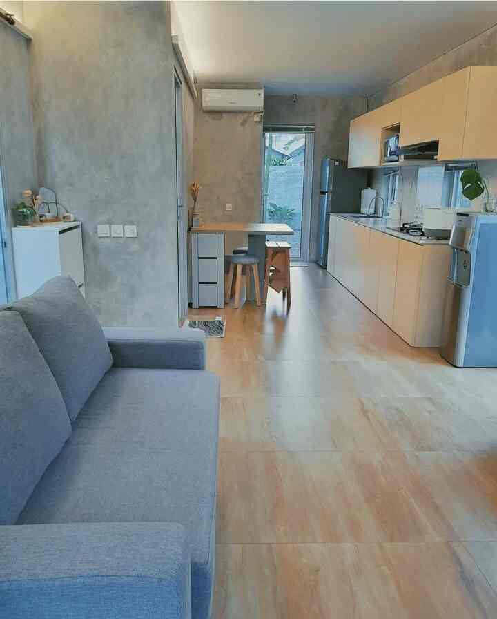 Wood tone flooring and gray sofa in a long, narrow open floor kitchen and living room space