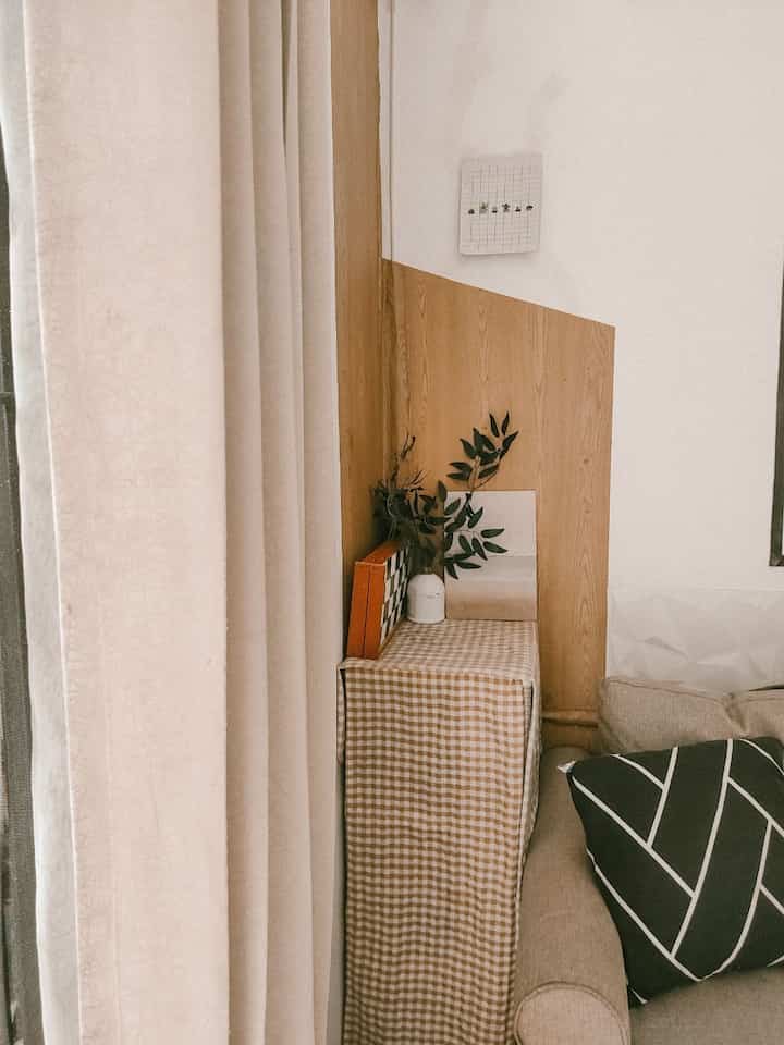 Beige and natural wood tone corner living room with checkered storage cabinet and cream curtains, creating a simple and comfortable atmosphere