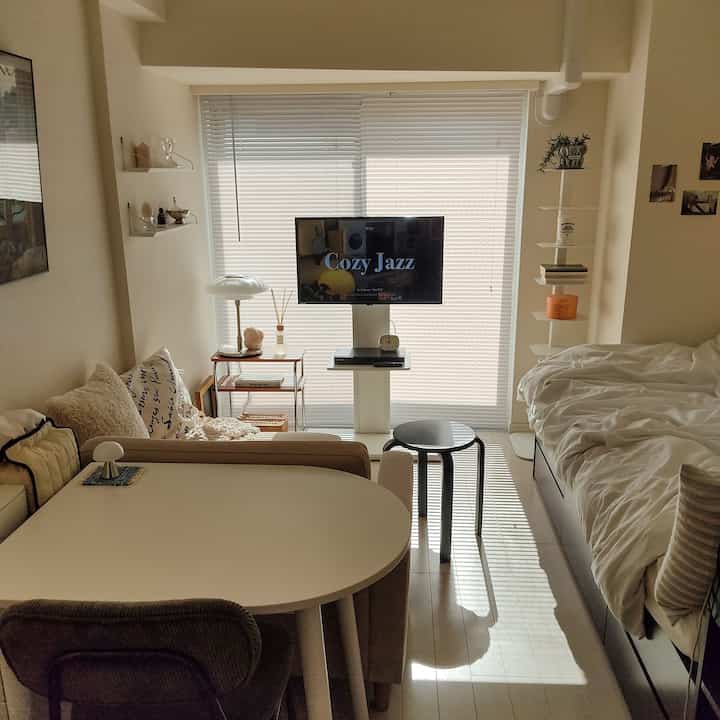 柔らかなベージュとホワイトのトーンの1Kワンルーム、ソファとベッド、テーブルランプが配置された温かみのある空間