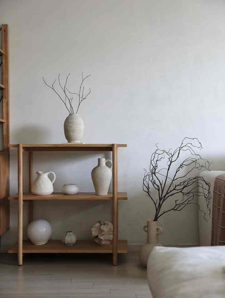 明るい白い壁と木目調の棚および床に配置されたシンプルな花瓶があるナチュラルなリビングルーム