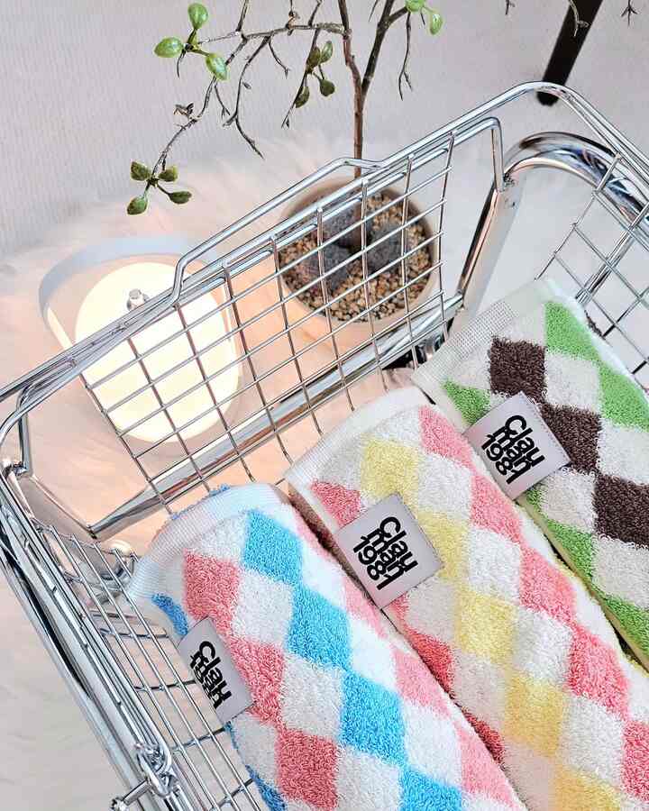 白とシルバートーンの空間、シルバーのバスケットにパステルカラーのアーガイル柄のタオルが並び、柔らかな光のテーブルランプが配置された雰囲気のあるインテリア