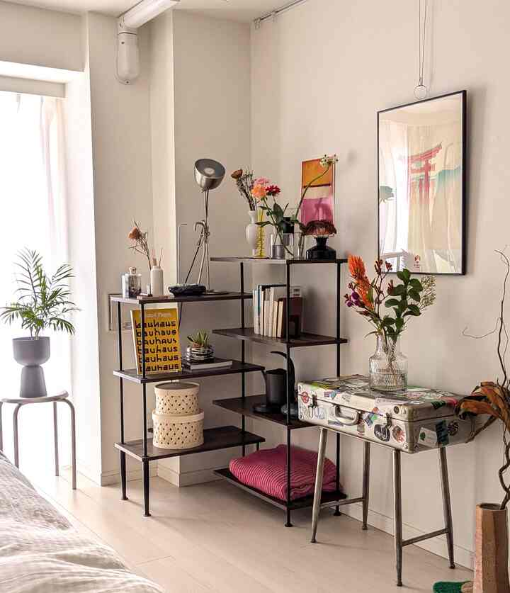 Light natural-toned living corner featuring black metal and wood rack with assorted vases, plants, and art posters in a modern setting