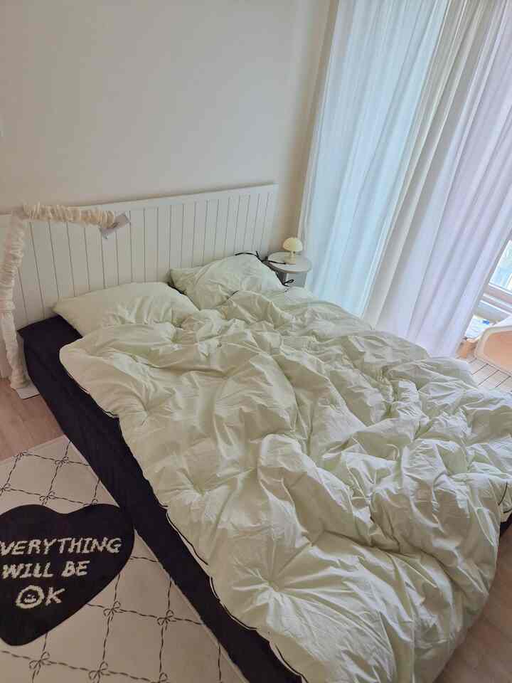 白を基調とした寝室、ベッドとナイトテーブル、白いカーテンが配置された自然な雰囲気のインテリア