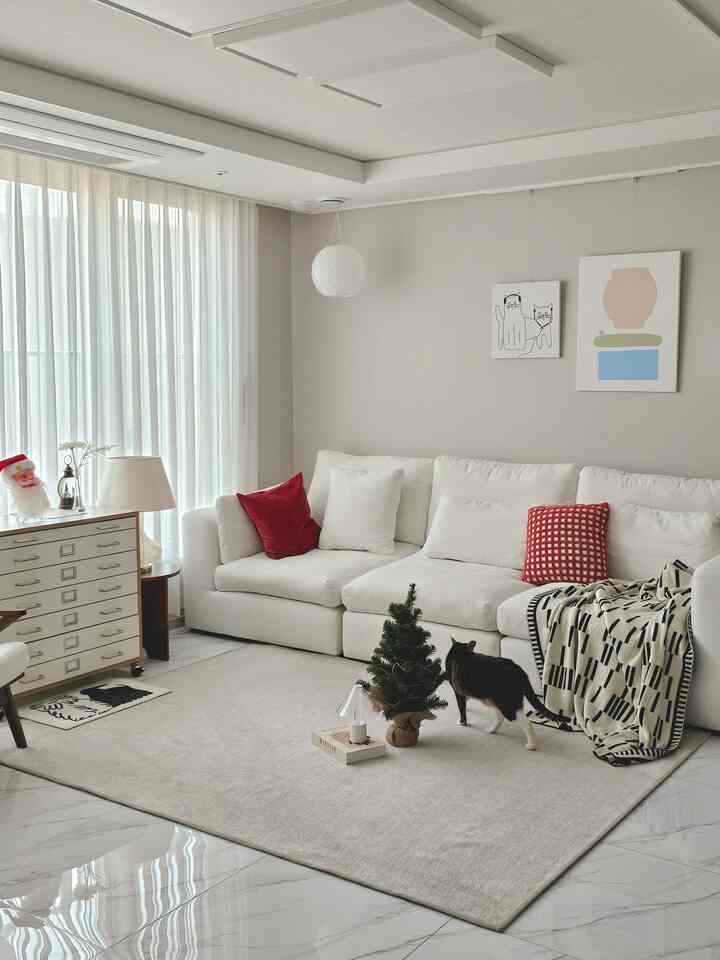 Bright white living room with red accents, featuring a mini Christmas tree, Santa decor, and a cat in a minimalist setting