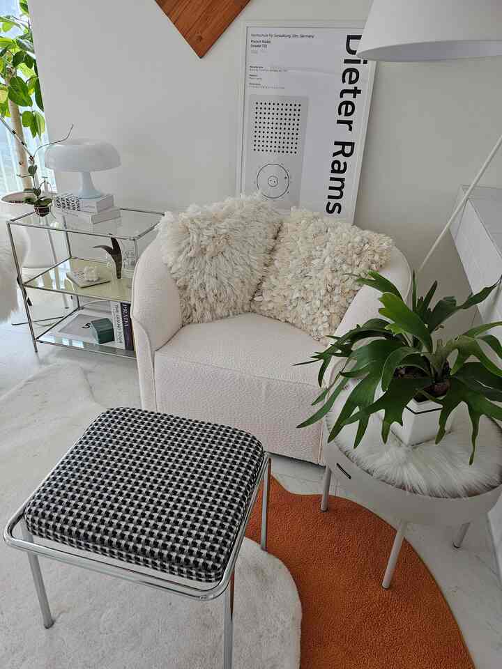 White and natural toned living room featuring mid-century modern sofa, stool, framed poster, and plants in cozy setting