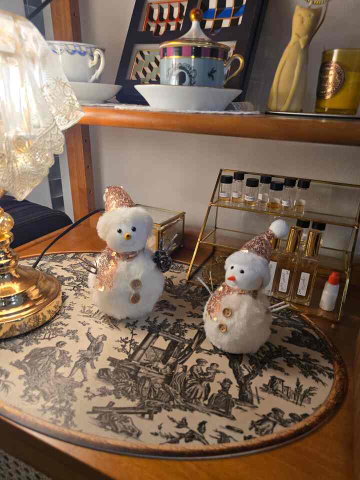 暖かみのあるブラウン木製テーブルにクリスマスの雪だるまオブジェとゴールドのアクセントがある香水瓶が置かれた雰囲気のあるインテリア