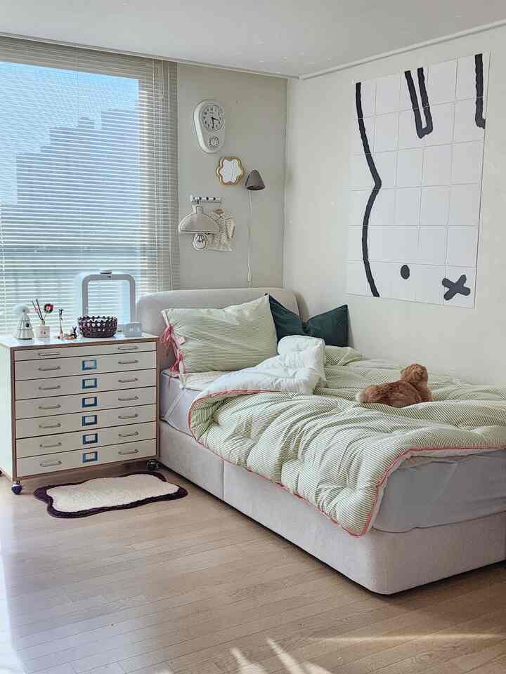 ホワイトとベージュのトーンの子供部屋、緑のストライプ寝具のベッドと収納チェストが配置された自然で居心地の良い空間