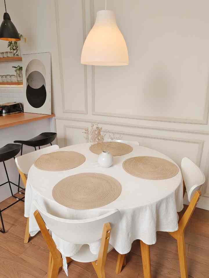White and wood tone 4-person dining room with a round table featuring placemats and vase, conveying a simple atmosphere