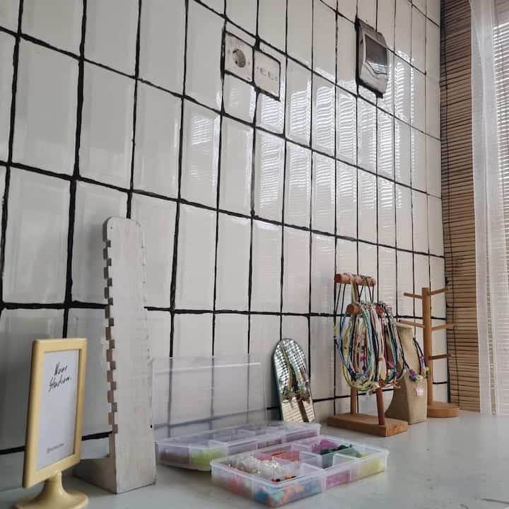 White and black tiled wall with jewelry stands and storage boxes on a craft workspace surface