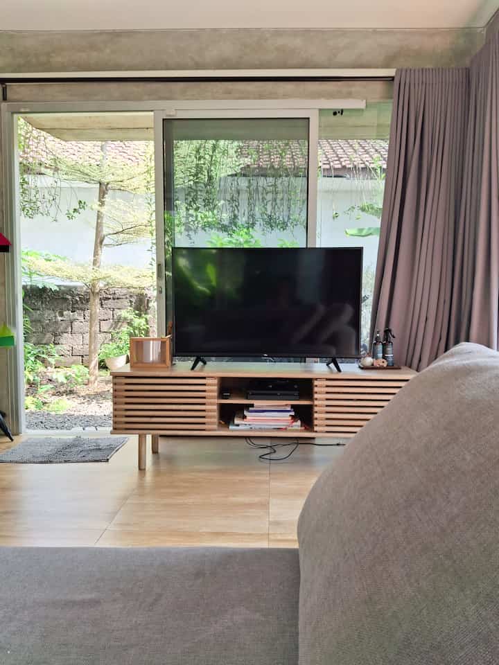 A natural wood tone and gray colored living room featuring a sofa bed and TV stand, reflecting a simple Japandi style space