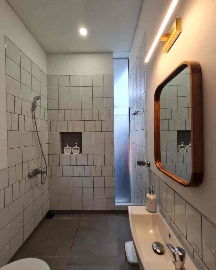 White and gray toned bathroom featuring modern tiled walls, sink, and wall lighting in a simple, clean design