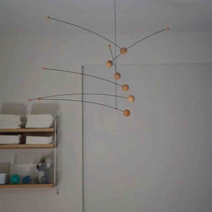 A white-walled living room corner featuring wood-toned shelves and a wooden ball mobile with a natural atmosphere