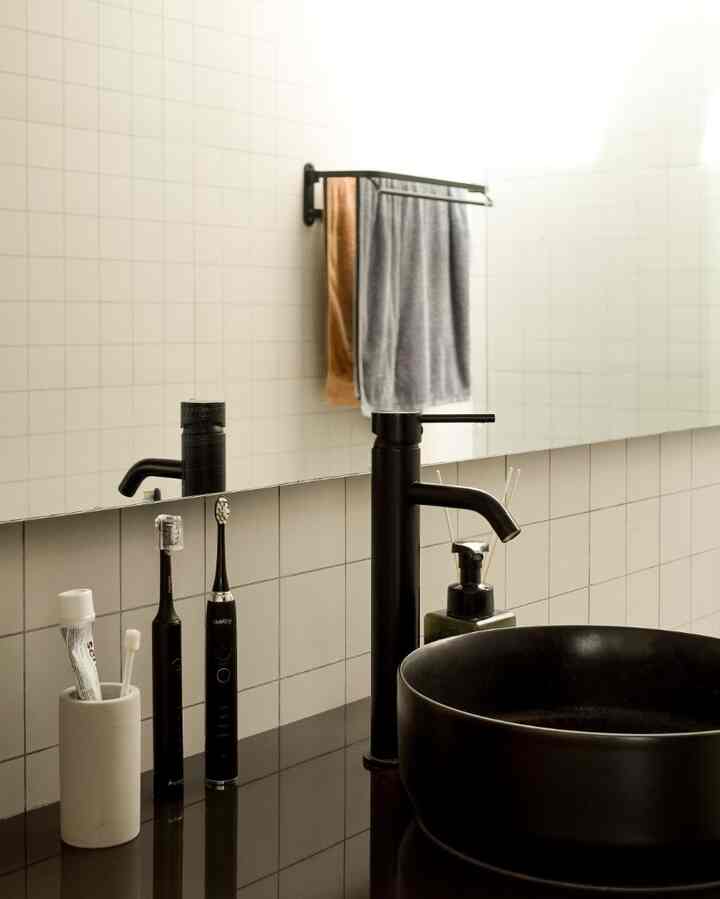 Clean bathroom vanity featuring white tiled walls, a black round washbasin, and matte black faucet