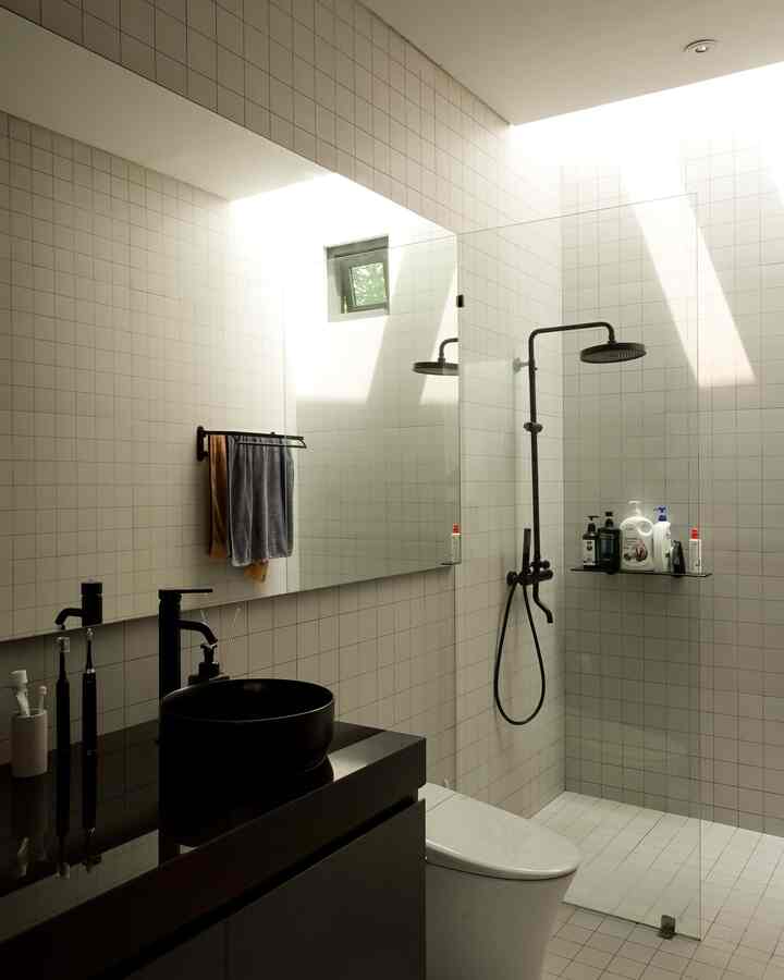 Modern bathroom with white tiled walls and floor, featuring black basin and shower with bright natural light