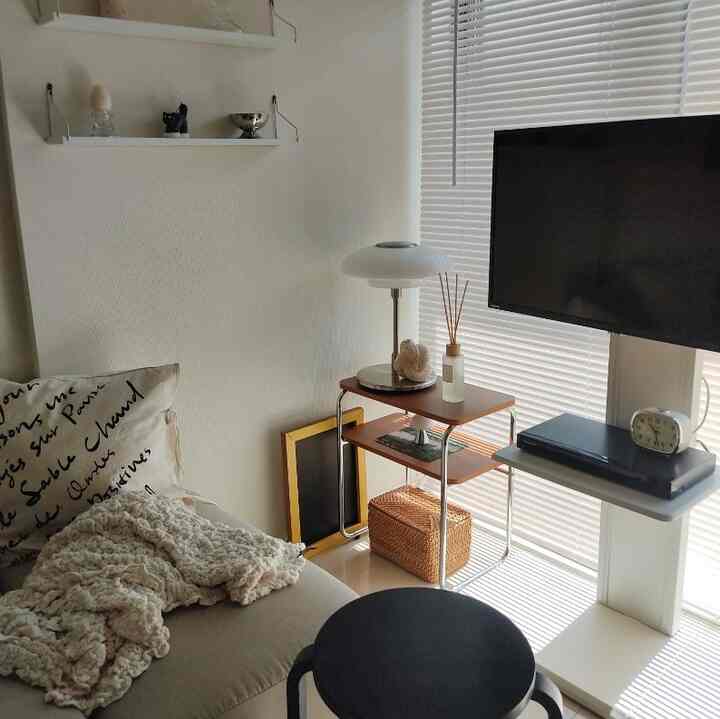 White and brown toned single household living room featuring sofa, table lamp, and TV stand with cozy atmosphere