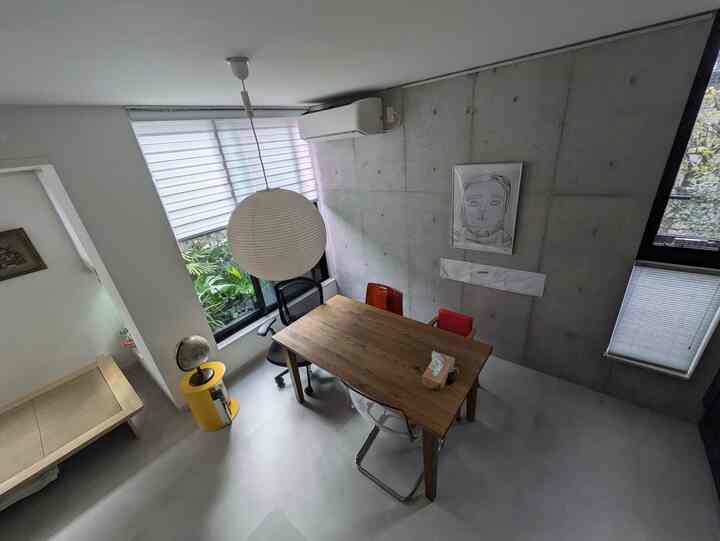 グレーのコンクリート壁と木製のダイニングテーブル、ペンダントライトが配置されたモダンなリビングルーム