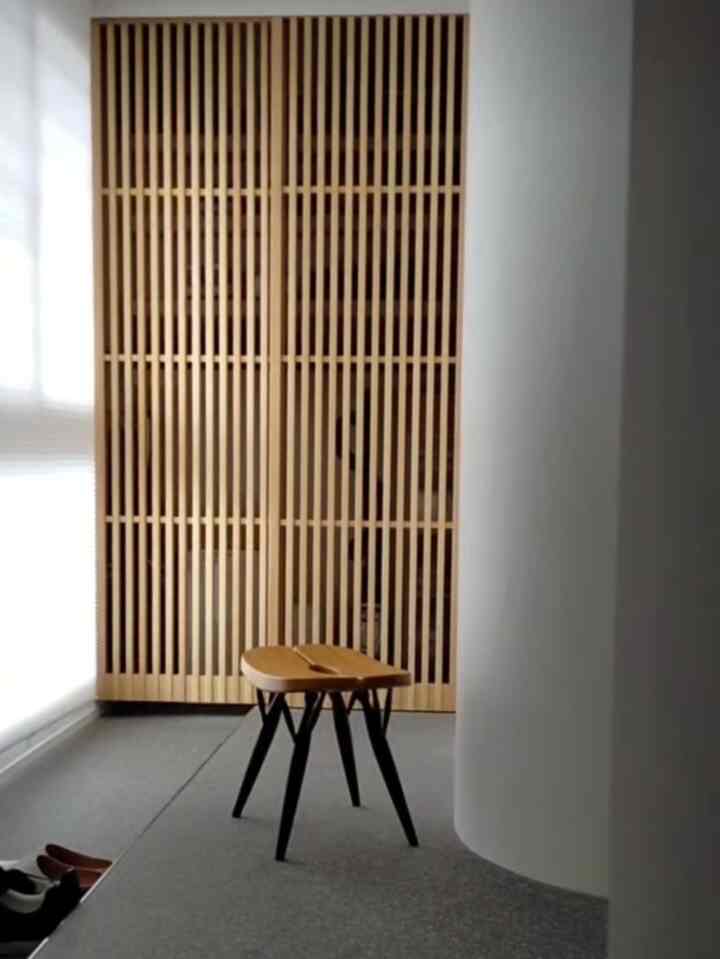 ナチュラルな木目調とグレーの床が調和する玄関、コンパクトな空間に収納家具とスツールが配置された雰囲気のあるインテリア