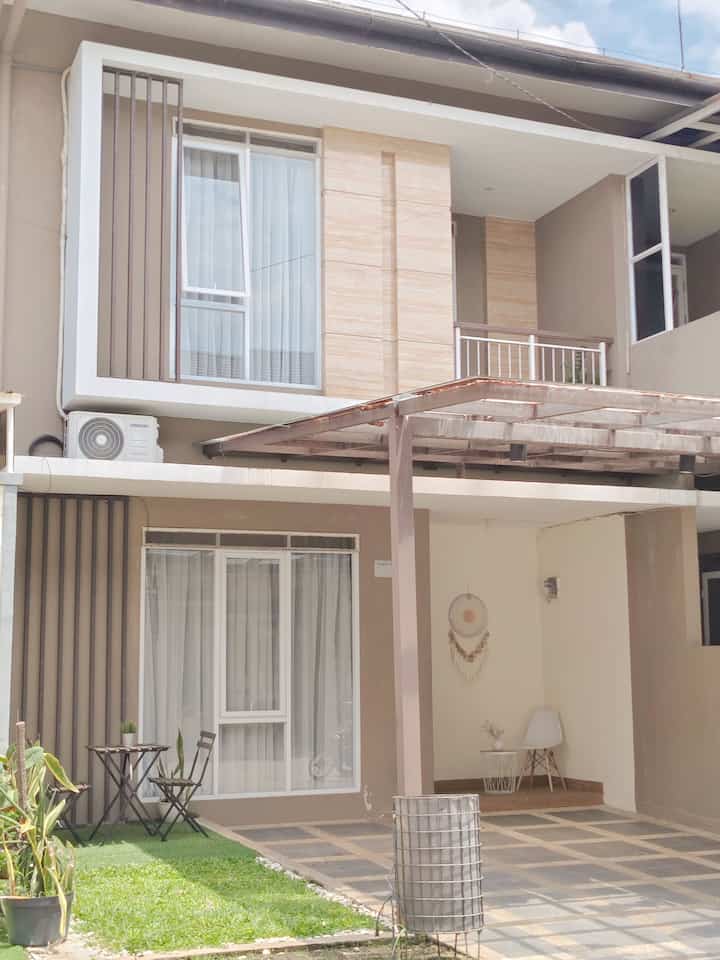 Natural toned house facade with glass canopy terrace, outdoor table, and green lawn creating a harmonious outdoor space