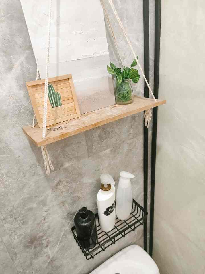 Natural toned bathroom wall featuring a wooden hanging shelf with plants and framed art, creating a simple and clean storage space