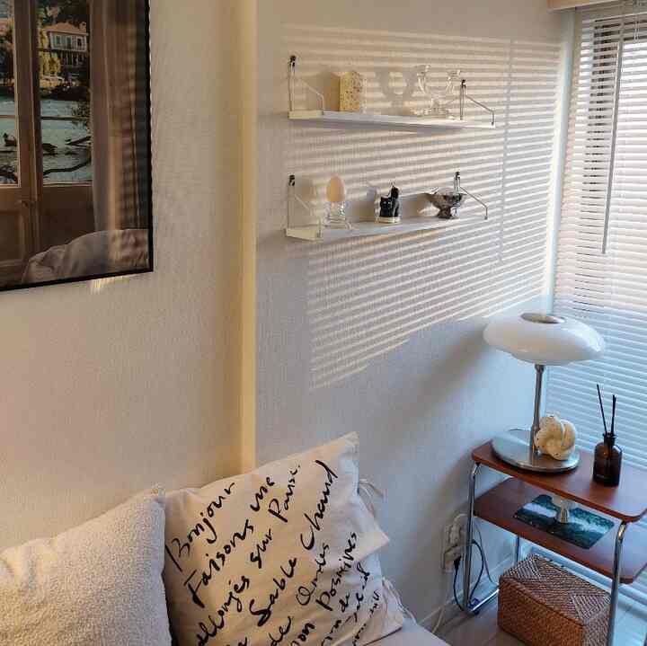 Natural tone single household living room with blinds casting striped light and a table lamp creating a cozy atmosphere