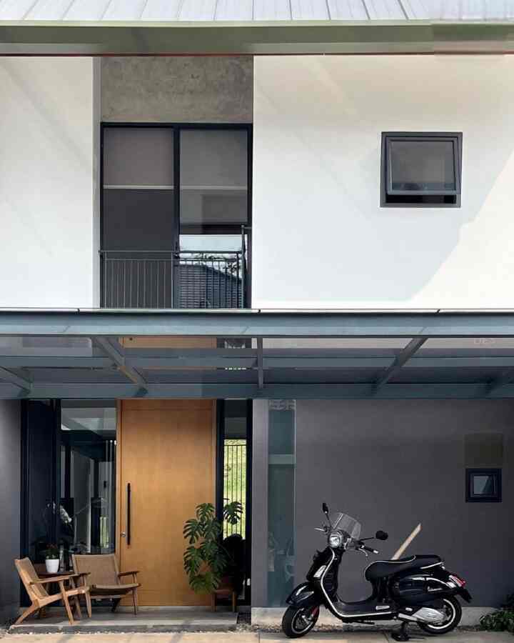 Modern exterior entrance of a house in white and gray tones, featuring wooden chairs, a potted plant, and a black scooter