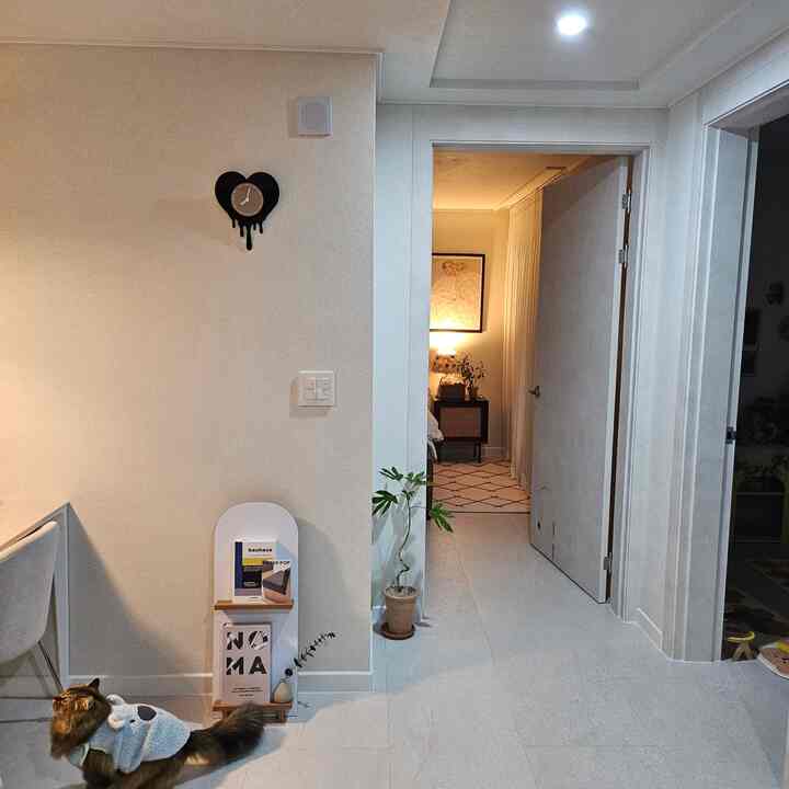 白色のモダンなリビングルーム、猫と植物、壁掛け時計、暖かい照明が配置された雰囲気のあるインテリア