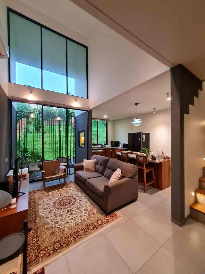 Bright white-walled compact living room and kitchen with high ceilings, featuring brown wooden furniture and a simple sofa in a natural modern style