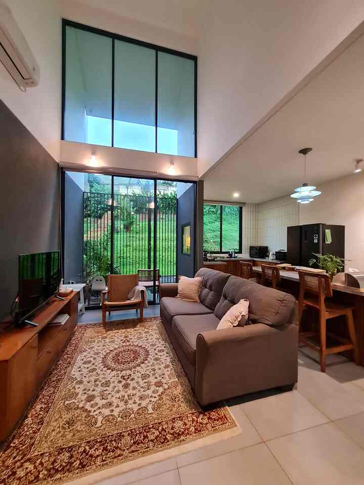 Modern open-plan living room and kitchen featuring a charcoal sofa and brown wooden furniture with large windows