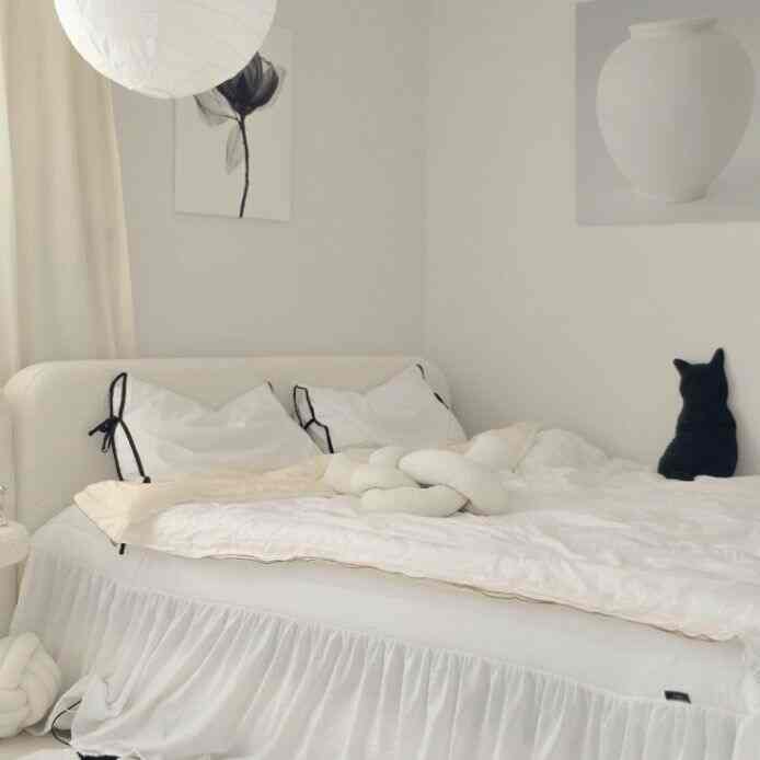 White-toned bedroom featuring a comfortable bed with cushions and a cat-shaped cushion creating a cozy atmosphere