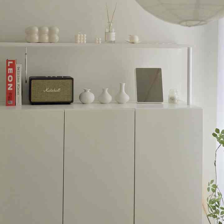 Bright white-toned living space featuring minimalist vases and candles neatly arranged on a shelf, creating a clean atmosphere