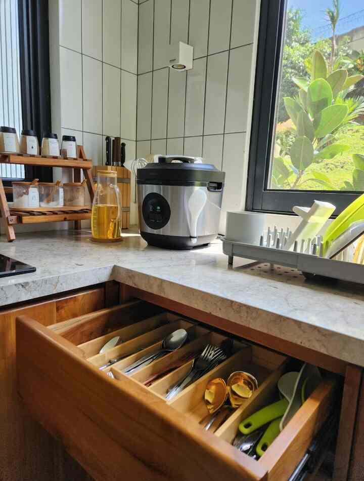 Natural wood and white tiled kitchen featuring an organized cutlery tray drawer and countertop kitchen utensils in a cozy atmosphere