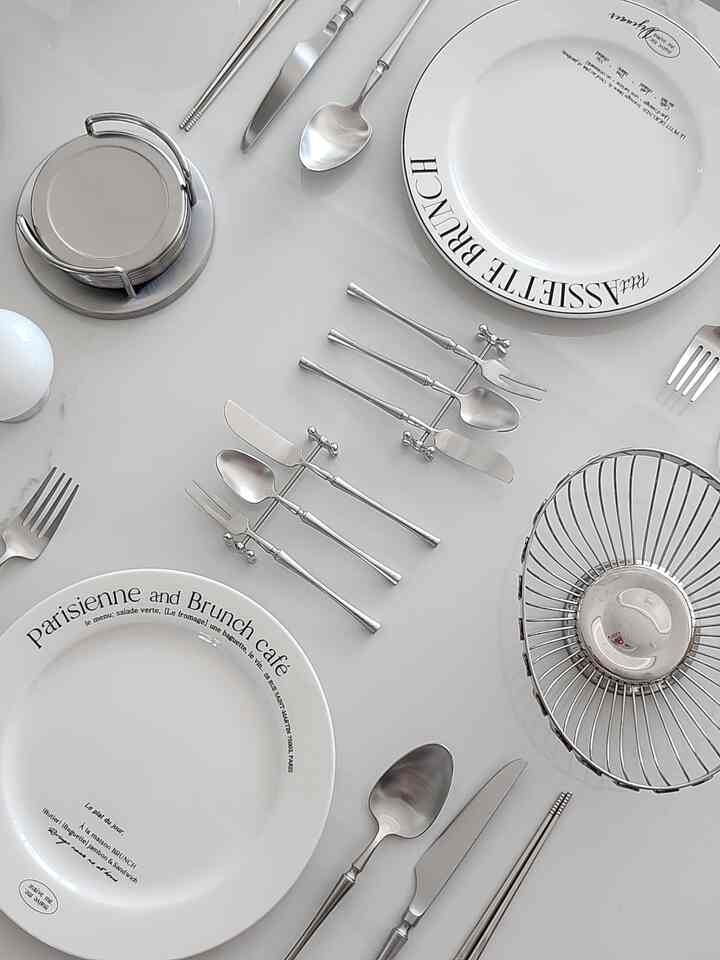 White and silver toned home cafe table featuring neatly arranged cutlery and lettering plates with a clean atmosphere