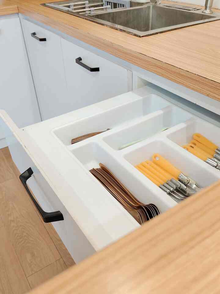 Wood tone kitchen countertop with white cutlery organizer holding rose gold and yellow-handled utensils in a neat space