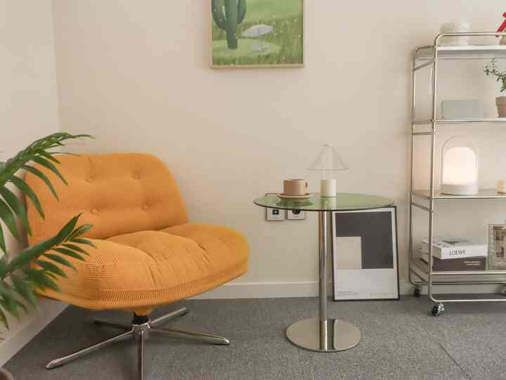 Cozy yellow single swivel sofa and round glass coffee table in a natural-toned small study space